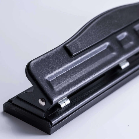 Side view of black adjustable two to three hole punch with padded handle, 11 sheet capacity for home or small office use on letter size docs.