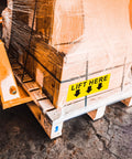 Front view of a pallet with shrink-wrapped boxes and a yellow 5x2 in Lift Here label decal with black arrows