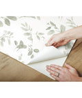 Hands peeling Dancing Leaves Peel And Stick Wallpaper Green And White for a quick easy wall makeover no glue needed removable
