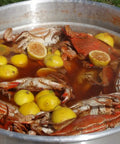 32-Quart Aluminum Boiling Pot With Punched Basket And Lid, Heavy Duty Construction With Sturdy Side Handles, Tailgate Ready Outdoor Jet Cooker Cookouts, Boiling Seafood, Corn, Crab And More filled with seafood boil including crabs and lemons