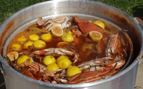 32-Quart Aluminum Boiling Pot With Punched Basket And Lid, Heavy Duty Construction With Sturdy Side Handles, Tailgate Ready Outdoor Jet Cooker Cookouts, Boiling Seafood, Corn, Crab And More filled with seafood boil including crabs and lemons