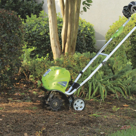 40V Cordless 10 Inch Tiller Cultivator With 4Ah Battery And Charger Included breaking up soil in a garden, showing green body and wheels.