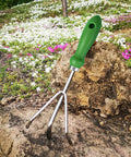 Three Tine Claw Garden Rake with ergonomic handle and stainless steel build resting on rock in the garden