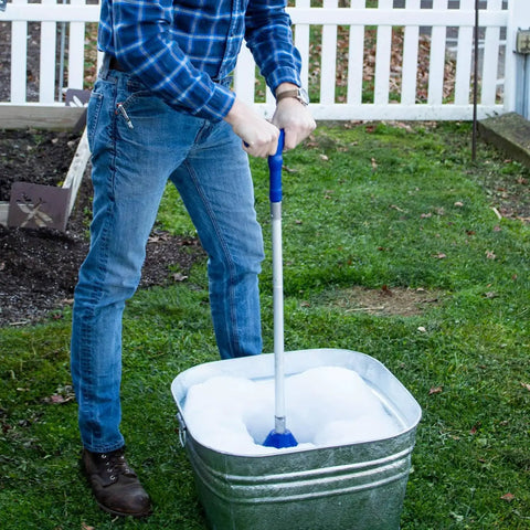 Portable Manual Clothes Washer Plunger working as a smooth washing agitator in bucket full of suds outdoors.