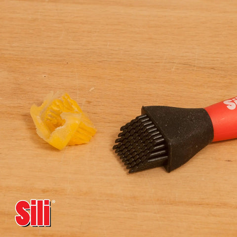 Silicone Glue Brush With One Inch Tip For Woodworking And Crafts next to peeled glue on wooden surface