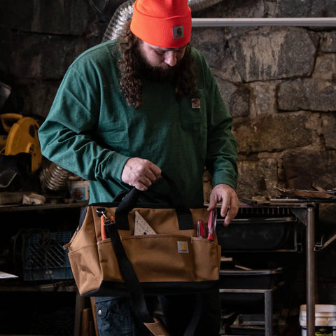 Person holding Trade Series 16 Inch Tool Bag with Zippered Main Compartment and 23 Pockets in a workshop setting