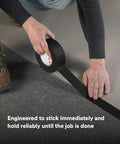 Person applying Extra Heavy Duty Industrial Duct Tape 6969, Gray, to carpet. Size 48 mm x 54.8 m, aggressive rubber adhesive.
