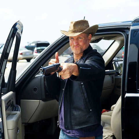 Man wearing an "Upcycled Tarp Hat From Brazil With Shapeable Brim And Ventilated Burlap Crown For Sun Protection Breathable Comfort And Trail Ready Outdoor Adventure For Weekend Warrior Style" standing by a black car, holding a rifle.