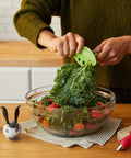 Person using Zero Stress Leaf Stripper For Fresh Kale And Collard Greens with greens in bowl, compact gadget for easy prep.