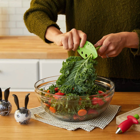 Person using Zero Stress Leaf Stripper For Fresh Kale And Collard Greens with greens in bowl, compact gadget for easy prep.