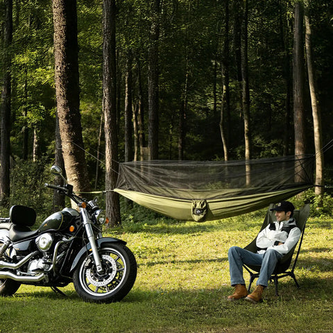 Man relaxing next to motorcycle with Bug Free Camping Hammock With Mosquito Net suspended in forest