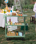 Flat Out Sturdy Three Tier Rolling Kitchen Cart Slick Green Metal Server with beverages and snacks in outdoor setting.