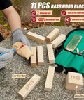 Person carving wood next to 11 basswood blocks, green roll-up bag, and strop from Beginner Friendly Wood Carving Set With 17 Tools Includes 3 Whittling Knives, 9 Basswood Blocks, Safety Gloves, Leather Strop Block, Polishing Compound, Roll Up Bag, And Clear Instructions For Adults Hobbyists.