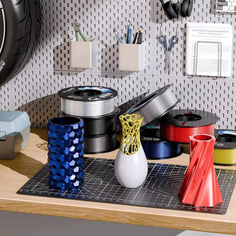 Various 3D printed vases with PETG 3D Printer Filament 1.75mm 1kg Army Green for Ender on a workshop table.