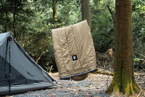 Ultralight Sleeping Quilt For Backpacking And Hammock Camping, 40 Degree Warmth With Footbox hanging between trees next to tent