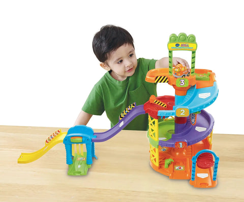 Child playing with Go Go Smart Wheels Spinning Spiral Tower Playset featuring levels, tracks, gas station, and car wash.