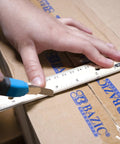 12 Inch Wooden Ruler With Inch And Metric Measurements Dual Scale being used to cut cardboard for precise lines.