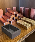 Front view of Nelyrho 4-piece graphite ingot mold set on a wood shelf with copper and gold ingots.