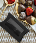 50 Pack Black Kraft Paper Pillow Gift Boxes With Window For Birthday Parties And Events next to chocolate covered strawberries