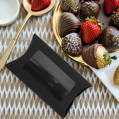 50 Pack Black Kraft Paper Pillow Gift Boxes With Window For Birthday Parties And Events next to chocolate covered strawberries