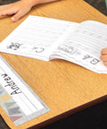 Student writing at desk with Classroom Cottage Flat Name Plates, 36 Pack, 11.5 X 3.5 Inches, Laminatable Labels.