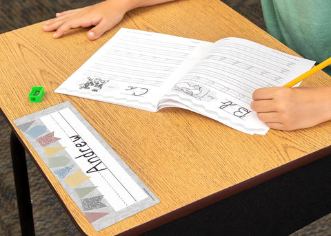 Student writing at desk with Classroom Cottage Flat Name Plates, 36 Pack, 11.5 X 3.5 Inches, Laminatable Labels.