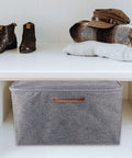 Grey storage box with handle under shelf, boots and folded clothes on shelf above.