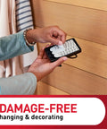 Person applying adhesive strips to XL Matte Black Triple Hook for damage-free wall hanging