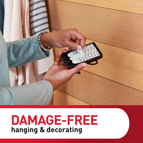 Person applying adhesive strips to XL Matte Black Triple Hook for damage-free wall hanging