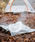 Emergency Fire Blanket 40 By 40 Inches, Woven Fiberglass Fire Shield covering a smoldering campfire in a forest setting.