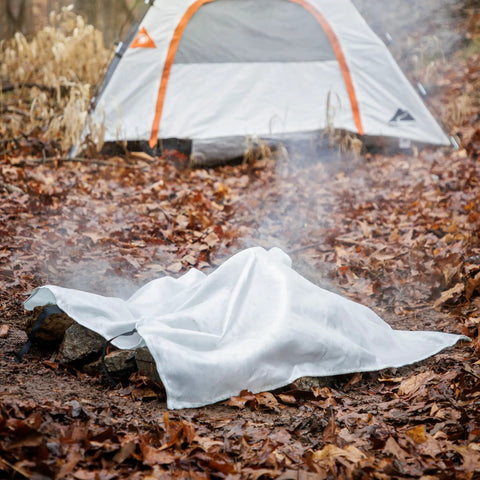 Emergency Fire Blanket 40 By 40 Inches, Woven Fiberglass Fire Shield covering a smoldering campfire in a forest setting.