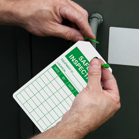 Hands attaching Top Shelf Safety Inspection Tags Paired With Adjustable Wire Ties For Quick Equipment Checks And Job Site Warning Labels.