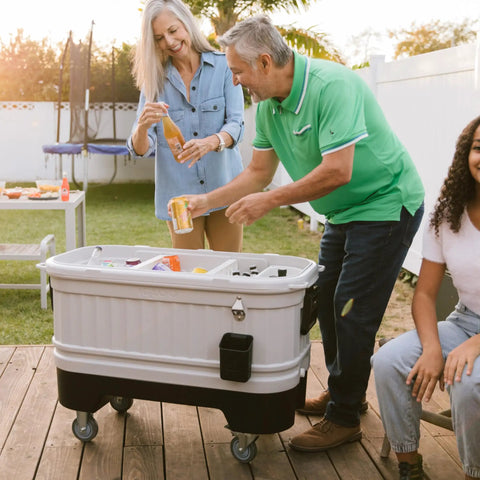 Adults using the 125 Qt Gray Party Bar Wheeled Cooler with Ultratherm Insulation, removable lid, and locking casters.