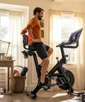 Man riding indoor bike with Oversized Bike Seat With Backrest For Peloton And Universal Bicycle Compatibility in home room