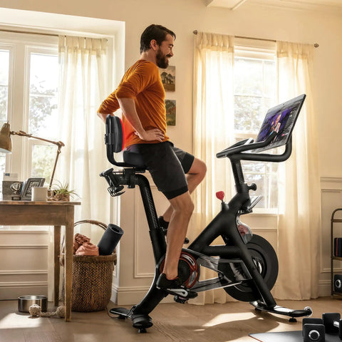 Man riding indoor bike with Oversized Bike Seat With Backrest For Peloton And Universal Bicycle Compatibility in home room
