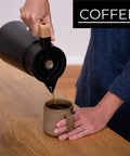 Person pouring coffee from 68 Oz Stainless Steel Insulated Coffee Carafe With Tea Infuser And Strainer 2 Liter Double Wall Vacuum Thermal Dispenser For Hot Or Cold Beverages Keeps Brew Fresh For Hours Black into a mug.