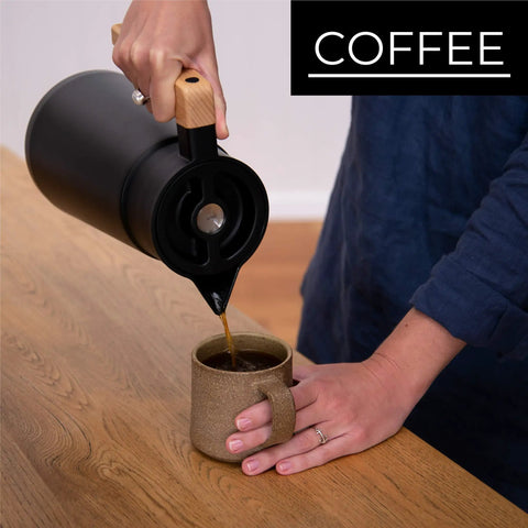 Person pouring coffee from 68 Oz Stainless Steel Insulated Coffee Carafe With Tea Infuser And Strainer 2 Liter Double Wall Vacuum Thermal Dispenser For Hot Or Cold Beverages Keeps Brew Fresh For Hours Black into a mug.