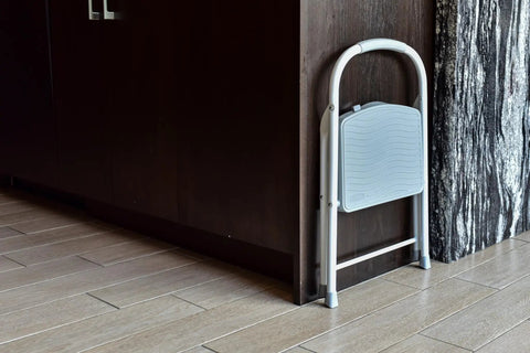 One Step Steel Folding Step Stool With Hand Grip And Traction Molded Steps, white and folded, stored beside a cabinet.