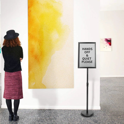 Adjustable Pedestal Poster Sign Stand For 8.5 x 11 Posters, Floor Standing Display With Aluminum Front Load Snap Open Reusable Frame, Tilts And Swivels For Quick No Fuss Viewing, Height Adjustable From 31.5 To 48 Inches, Black, placed in art gallery.