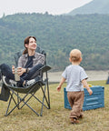 Person sitting in Oversized Folding Camping Chair With High Back Padded Comfort, outdoors, with child playing nearby