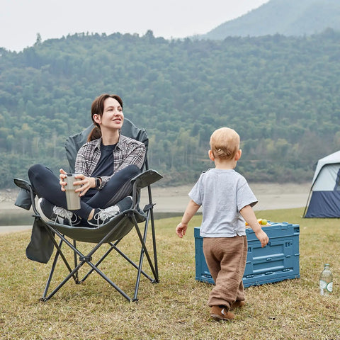 Person sitting in Oversized Folding Camping Chair With High Back Padded Comfort, outdoors, with child playing nearby