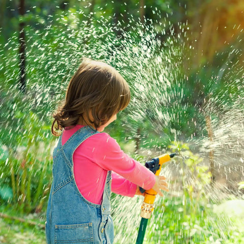 Child playing with water hose in garden, showcasing Eight Piece Three Quarter Inch Garden Hose Quick Connectors Set Made From Solid Brass No Leak