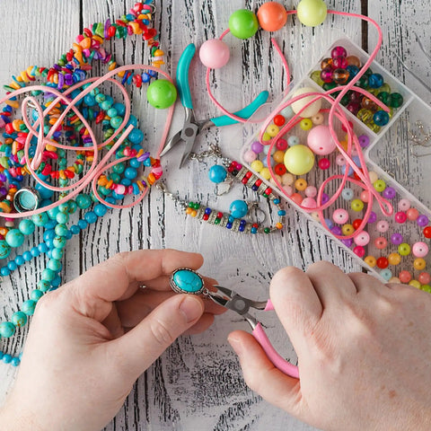 Hands using 4 Piece Jewelry Pliers Set For Beading And Jewelry Making Including Needle Nose Pliers, Round Nose Pliers, Bent Nose Pliers And Wire Cutter Handy Tools Kit For Bracelet Craft, Wire Wrapping, And DIY Jewelry with colorful beads on table