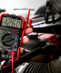 Hand holding Auto-Ranging Digital Multimeter For Automotive And Home Electrical Troubleshooting UL Certified near car engine