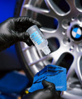 Applying Rim EVO 30ml Ceramic Wheel Coating Kit to blue cloth near silver car rim, high heat resistant up to 1400°F.