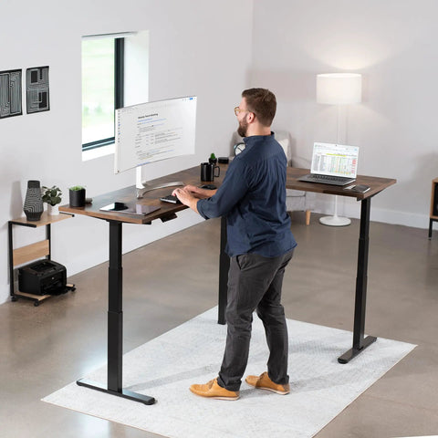 Man working at Electric Triple Motor Height Adjustable Corner Desk Frame For L Shaped Setup With 3 Legs Sit Stand Ergonomic Frame Up To 300 Lbs Black Frame Only DESK V130EB