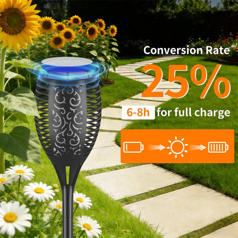 Solar torch light with realistic flickering flame in a garden setting, near a pathway with daisies and sunflowers. Six Pack Solar Torch Lights With Realistic Flickering Flame For Outdoor Yard Pathway Garden Patio Waterproof Tiki Torches For Halloween Party Decor And Backyard Ambience.