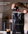 Person recycling coffee capsules with Vertuo Plus Single Serve Coffee And Espresso Maker With Aeroccino Milk Frother Ink Black in background