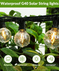 Close-up of 100Ft Solar String Lights With 52 LED Globe Bulbs, Warm 2700K Glow, shatterproof bulbs in outdoor greenery setting.