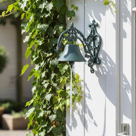 Badass Heavy Duty Cast Iron Outdoor Wall Bell With Slick Vintage Rustic Patina mounted on white wall surrounded by ivy.